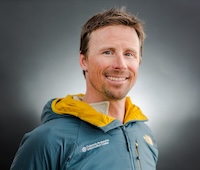 headshot of Kreston wearing a blue CAIC jacket in front of a gray backdrop