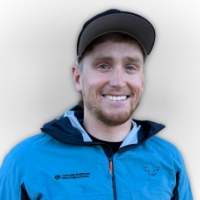 Luke Robinson, CAIC Field Technician Central Mountains at CAIC, smiling and wearing a blue jacket against a light grey background.
