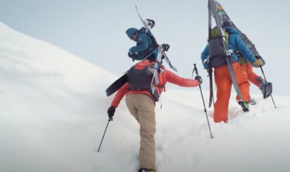 People with skies hiking up snow covered mountain