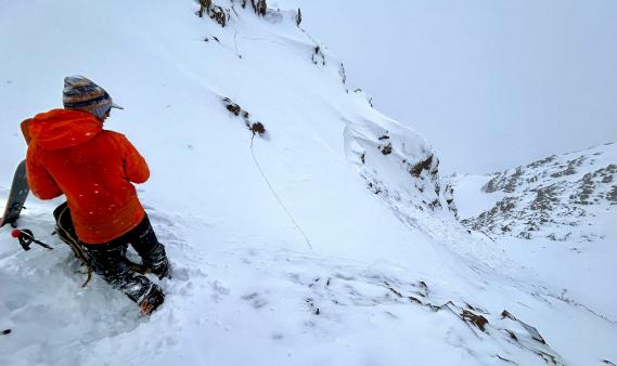 Skier in red coat looking downhill at small wind slab avalanche
