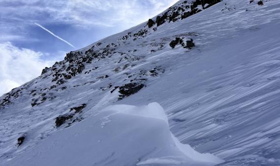 close-up of a wind slab avalanche crown below some rocks under a moody sky. 