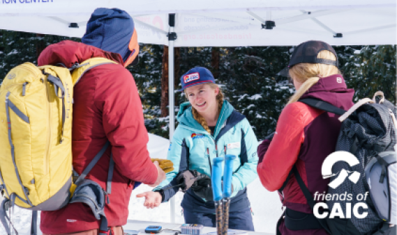 Friends of CAIC staff member under tent talking to people with backpacks in the snow