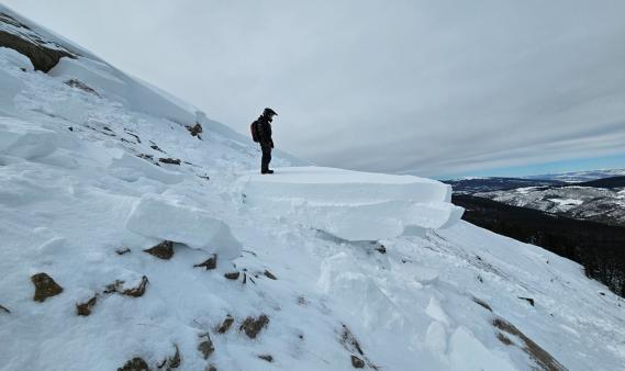 A person standing with a backpack amidst avalanche debris.