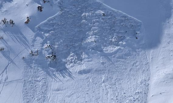 Looking straight on at a slope with a large avalanche on it, starting in a rocky area.