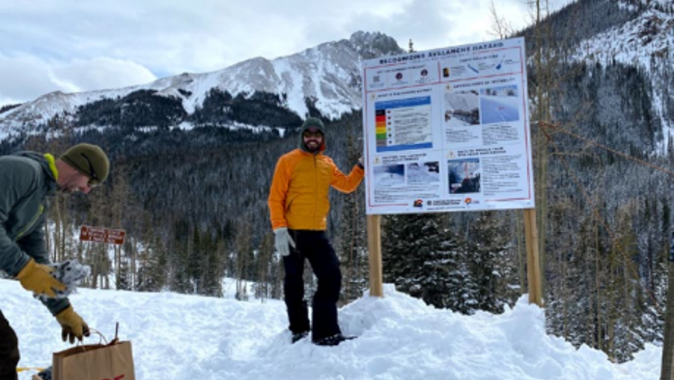 photo of man standing next to sign on top of snow pile