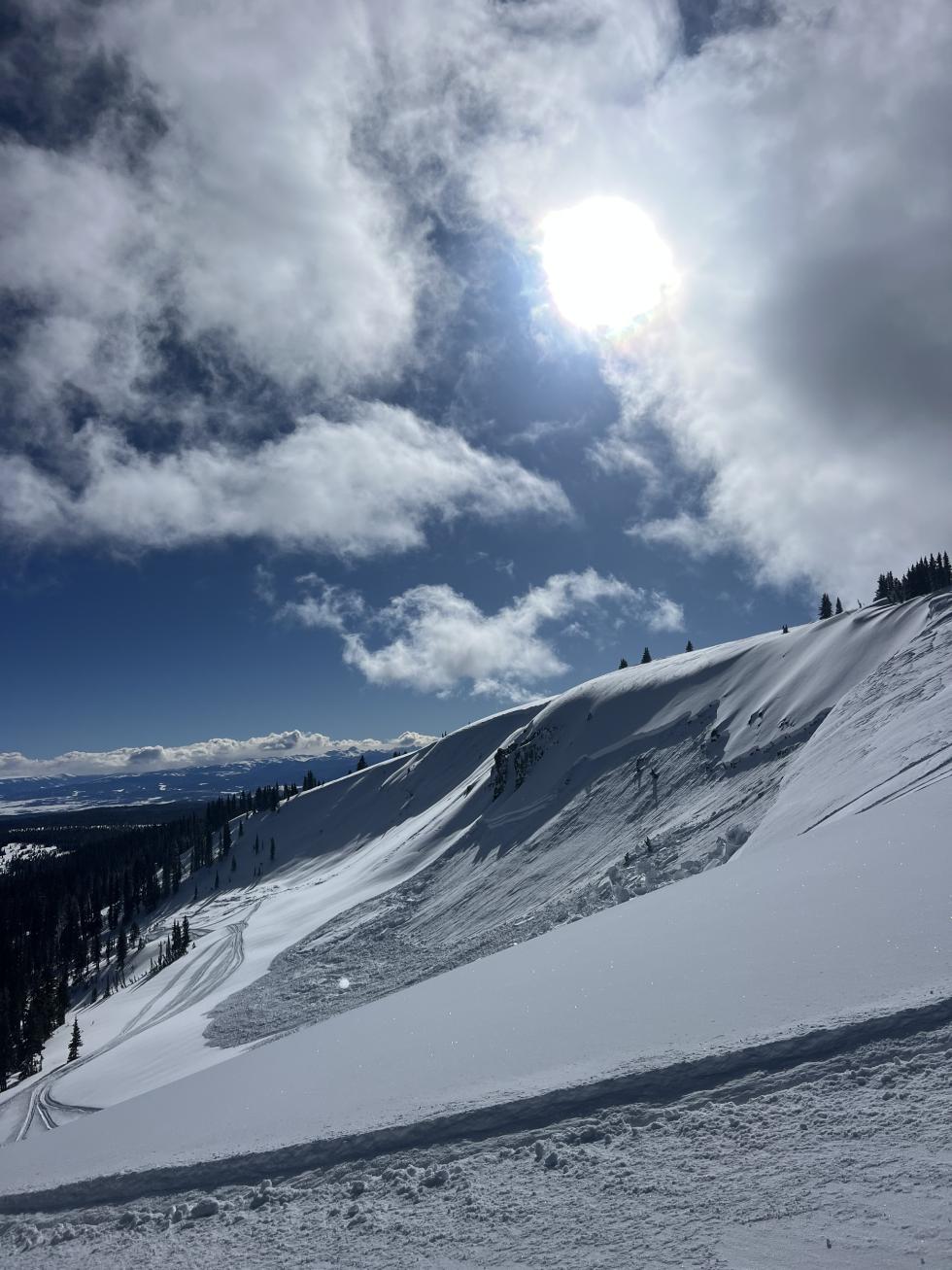 large avalanche in the distance with a track below the slope.