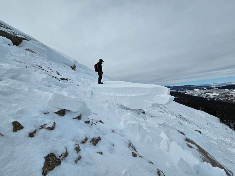 A person standing with a backpack amidst avalanche debris.