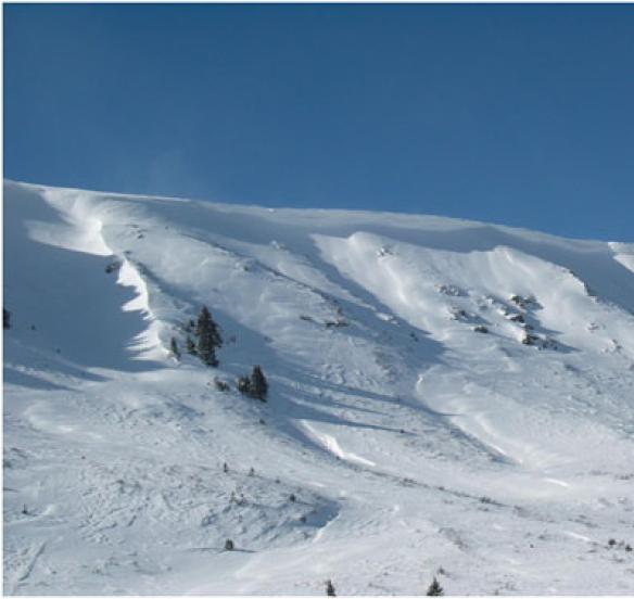 A corniced ridgeline. A large cornice has formed at the top of the ridge. A smaller cornice has formed to the left of the trees from crossloading.